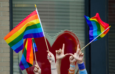 Cropped hands of women holding rainbow flags in city