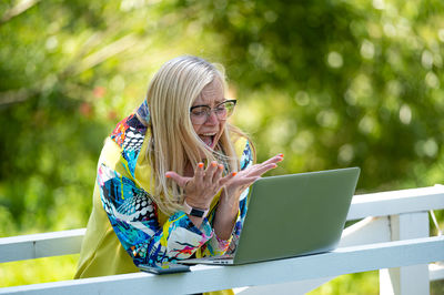 Senior emotional woman with laptop making video call and actively gesturing, online communication