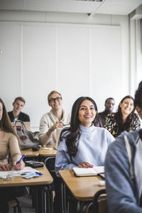 Multi-ethnic smiling male and female students sitting at desk in classroom