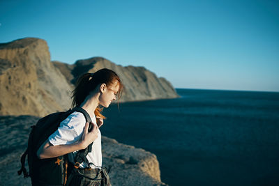 Man standing on rock by sea against clear sky