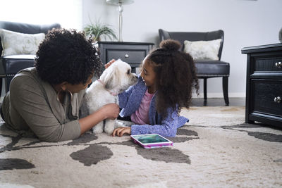 Mother and daughter playing with lhasa apso while lying on rug at home