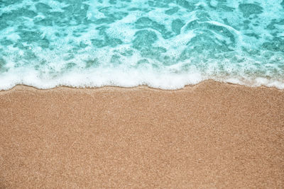 Abstract summer background, soft wave-covered sand beach with blue water.