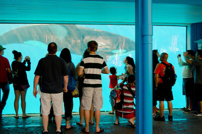 People looking at killer whale swimming in fish tank at aquarium