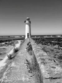 Lighthouse on beach by sea against sky