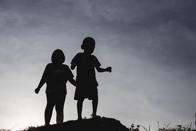 Low angle view of silhouette friends standing against sky