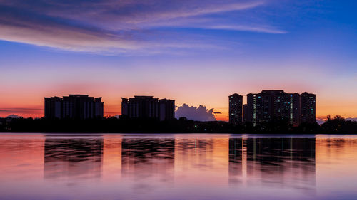 Lake and buildings against sky during sunset
