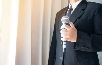 Midsection of man holding camera while standing against wall