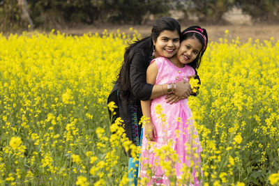 A pretty indian mother hugging her daughter and standing in yellow mustard flower field