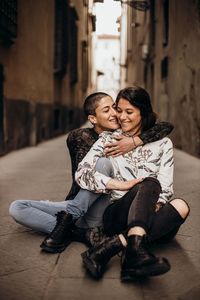 Happy lesbian couple sitting at alley in city