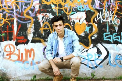 Full length of young man sitting against graffiti wall