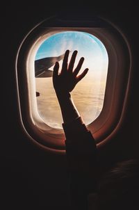 Cropped hand touching window while traveling in airplane