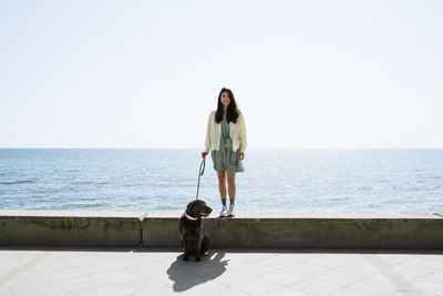 Happy woman with dog standing on retaining wall in front of sea