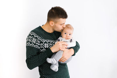 A young father holds his little son in his arms and kisses him on a white background