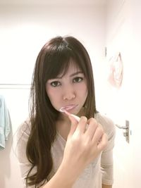 Portrait of beautiful young woman brushing teeth in bathroom