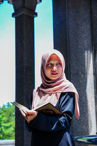 Young woman wearing hijab while reading holy book at mosque