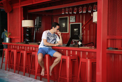 Full length of man sitting on red building