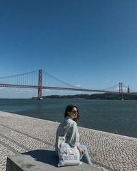Girl sitting on the embarkment of lisbon with red bridge on the backgroun