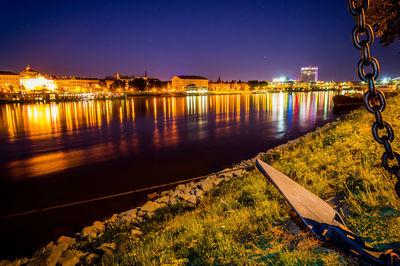 Illuminated cityscape by river against sky at night