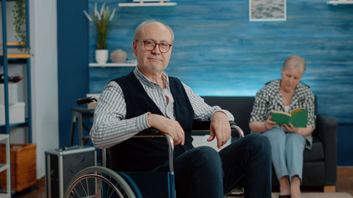 Portrait of man sitting in wheelchair while woman read book in background