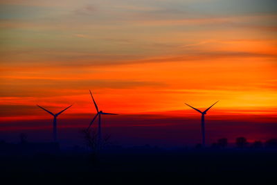 Silhouette wind turbines on landscape against orange sky