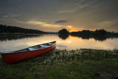 Boat moored on river against sky during sunset