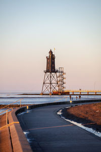 Lighthouse amidst sea against clear sky during sunset