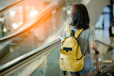 Rear view of woman with luggage standing on moving walkway
