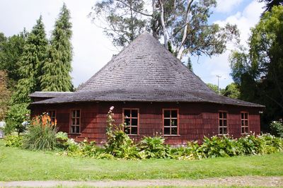 House amidst trees and plants on field against sky