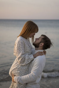 Side view of couple standing at beach against sky