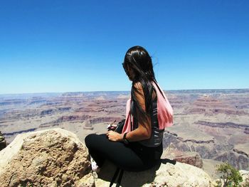 Woman sitting on mobile phone against clear sky