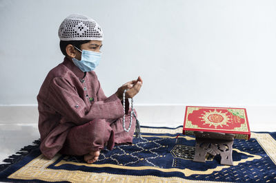 Full length of boy wearing mask praying at home