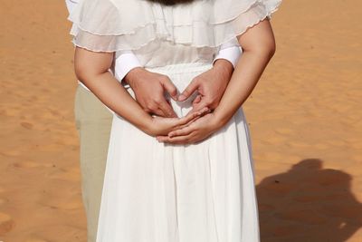 Midsection of couple making heart shape at beach