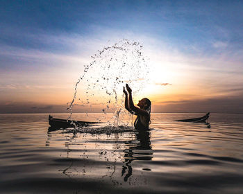 Silhouette person in sea against sky at sunset