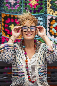 Portrait of young woman wearing sunglasses standing against wall