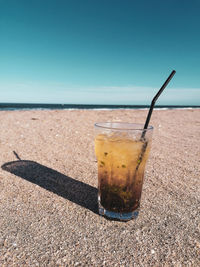 Glass of water on beach against sky