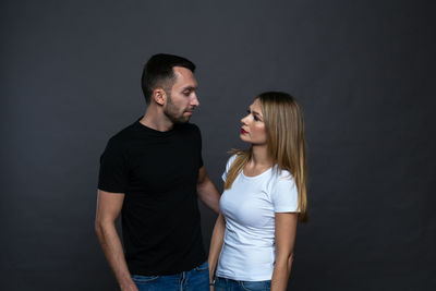 Couple looking at each other while standing against gray background