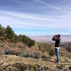 Side view of man looking through binocular while standing on field against sky