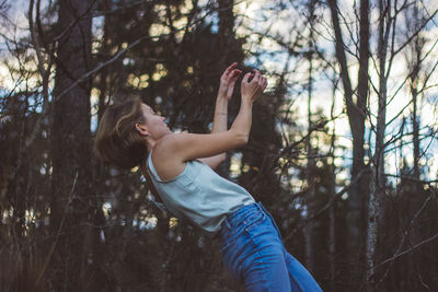 Side view of young woman dancing against trees in forest