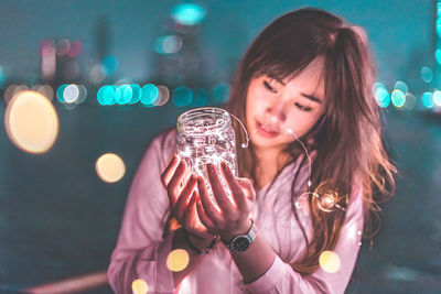 Young woman holding illuminated lights in jar