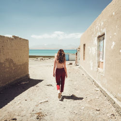 Rear view of woman walking on building by sea against sky