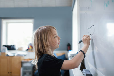 Side view of serious girl drawing on whiteboard in classroom