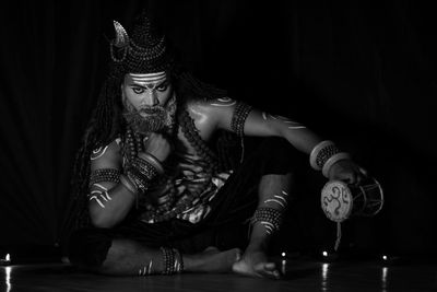 Portrait of man wearing shiva costume while sitting in darkroom