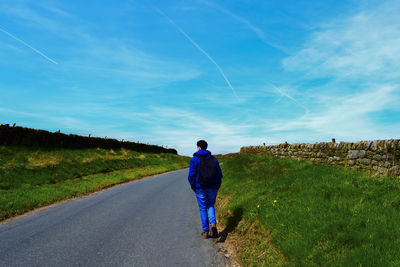 Rear view of man walking on road against sky