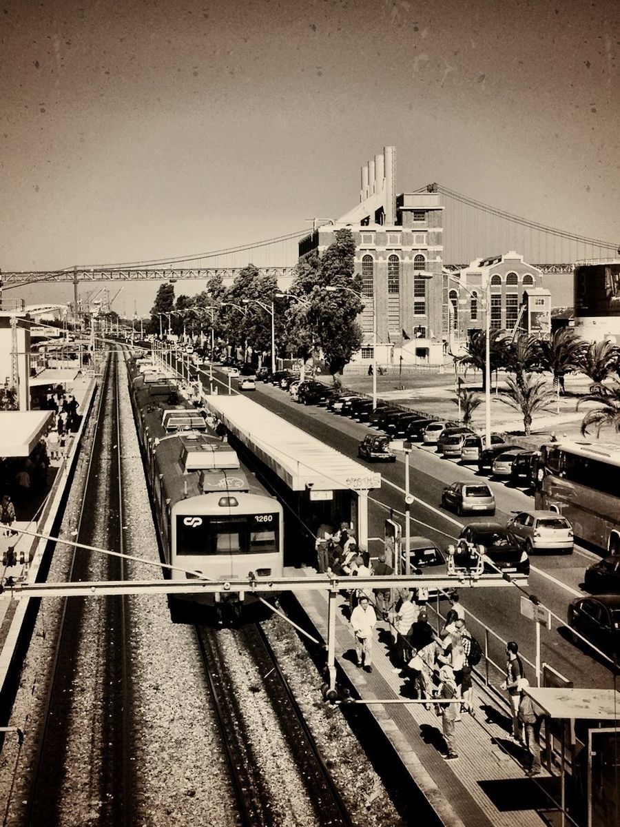 transportation, building exterior, architecture, built structure, railroad track, city, high angle view, public transportation, mode of transport, rail transportation, city life, railroad station platform, railroad station, car, land vehicle, clear sky, incidental people, street, travel, city street