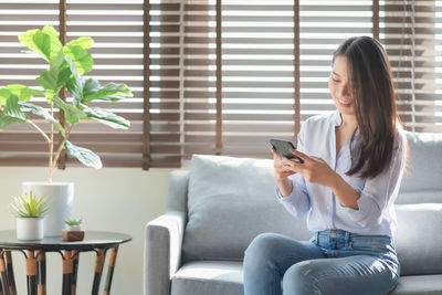 Young woman using phone while sitting on sofa at home