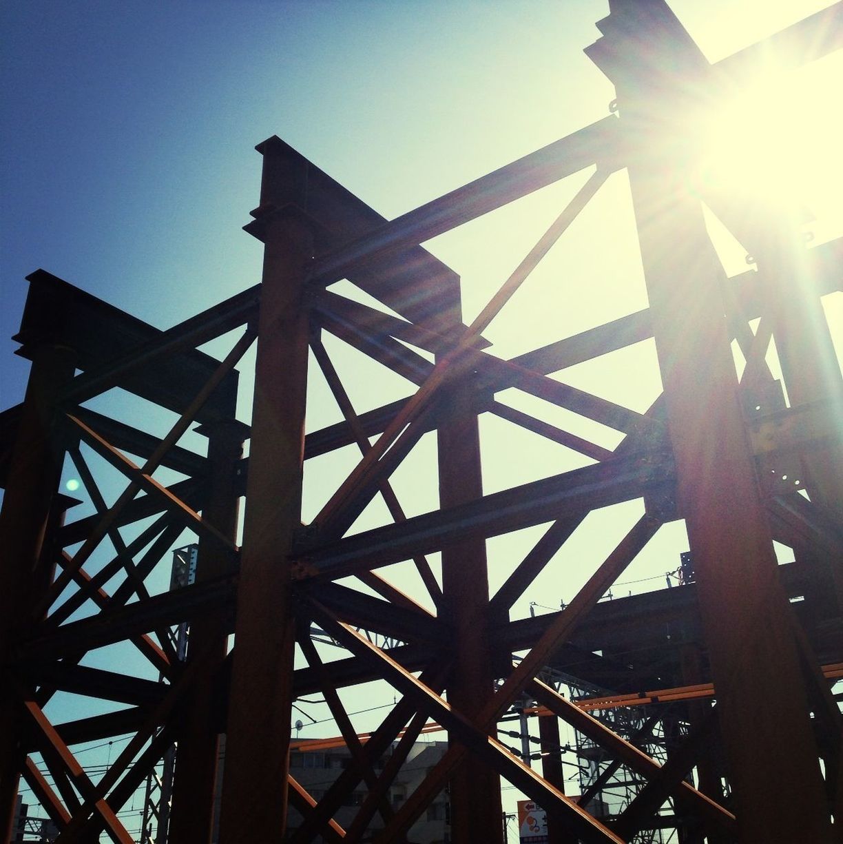 low angle view, sun, sunlight, built structure, sunbeam, metal, lens flare, clear sky, engineering, architecture, metallic, sky, connection, bridge - man made structure, silhouette, construction site, outdoors, no people, sunset, blue