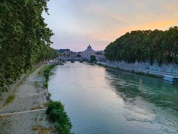 River amidst buildings against sky at sunset