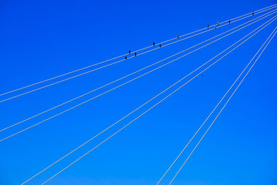 Low angle view of power lines against clear blue sky