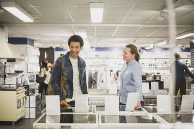 Smiling mature owner talking to male customer in electronics store