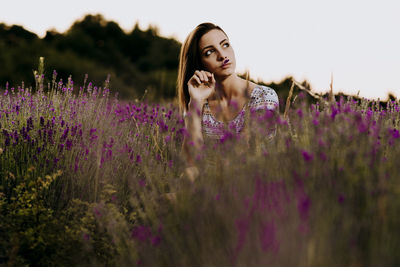 Beautiful woman standing on field by purple flowering plants against sky